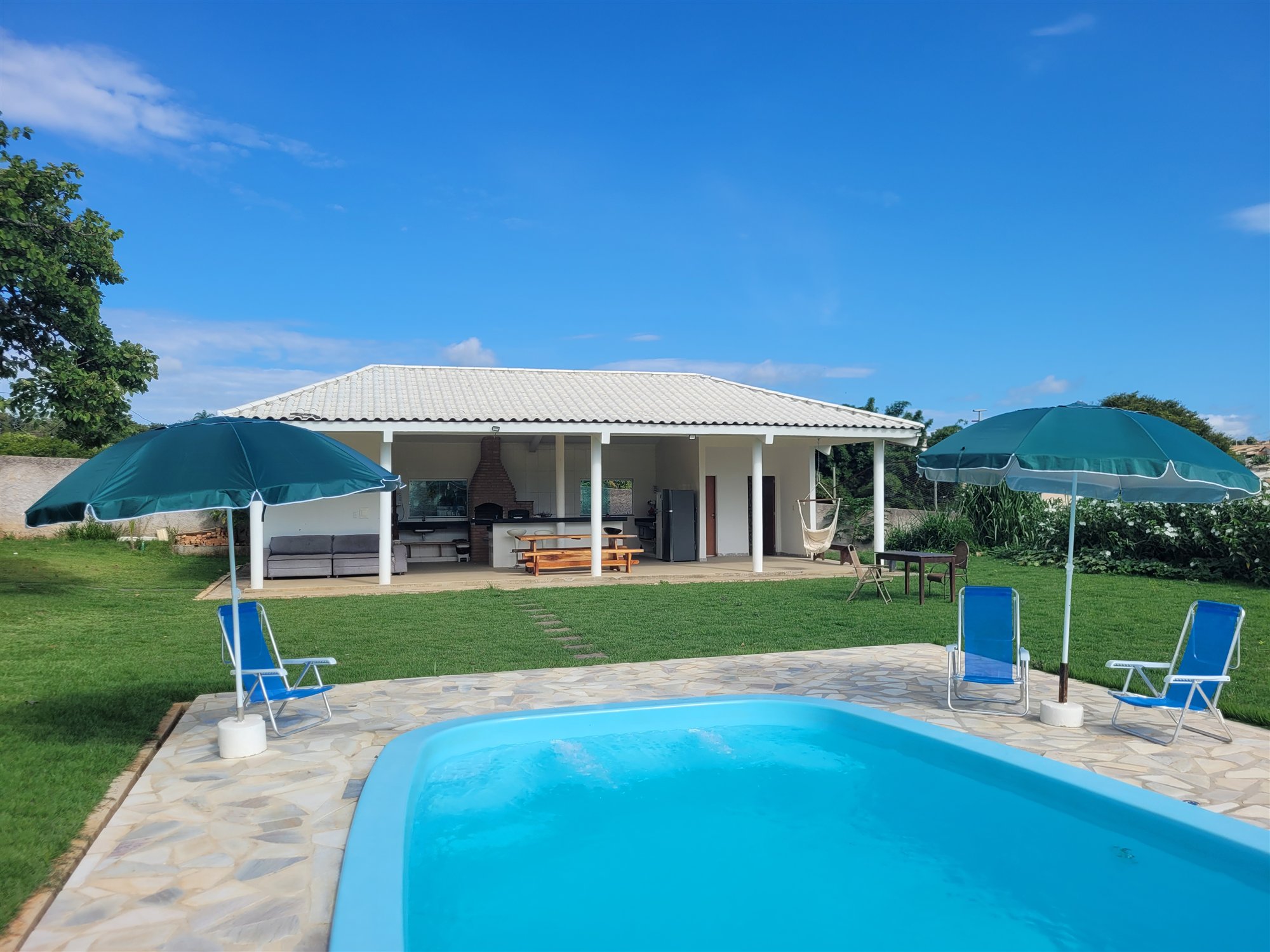 Piscina diante de uma área verde ampla e da cozinha aberta